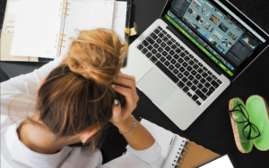 A stressed woman sitting in front of her computer, holding her head in her hands, reflecting deep frustration and exhaustion.