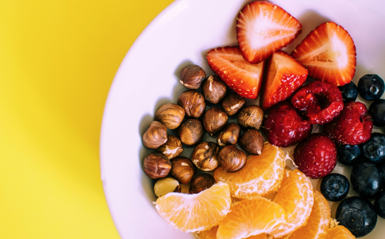 An array of colorful fruits and vegetables, including strawberries, oranges, bananas, leafy greens, and carrots, arranged artfully on a rustic wooden table. The vibrant colors highlight the diversity of plant-based diets, emphasizing fresh, healthy eating. The image symbolizes the journey from a vegan to a fruitarian diet, showcasing the variety of choices available within plant-based living.