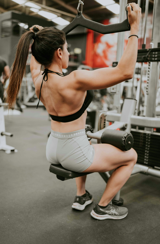 A woman performing Lat Pulldown on a machine at the gym, building a strong upper back to get the hourglass figure illusion.