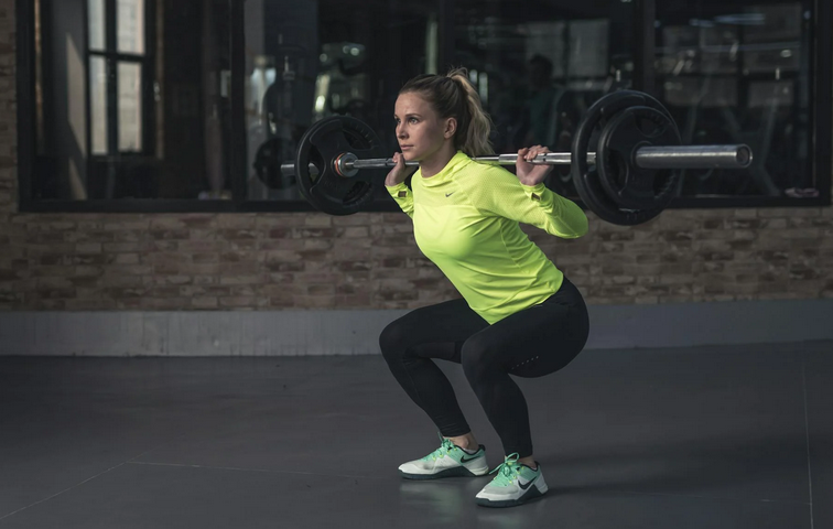 A woman performing squats with a bar and weights at the gym, building a stronger lower body.