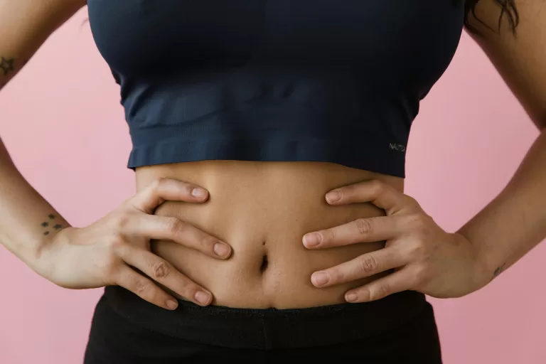 A woman standing wearing a black crop top touching her stomach.