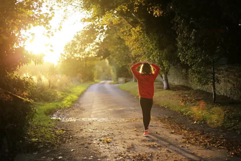 A woman walking on the street in fitness clothes while the sun is shining.