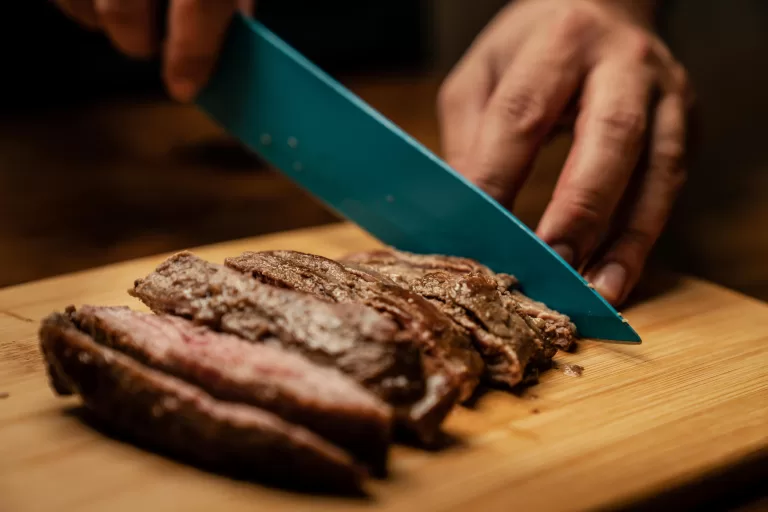 A person cutting up a piece of freshly baked meat on a wooden cutting board.